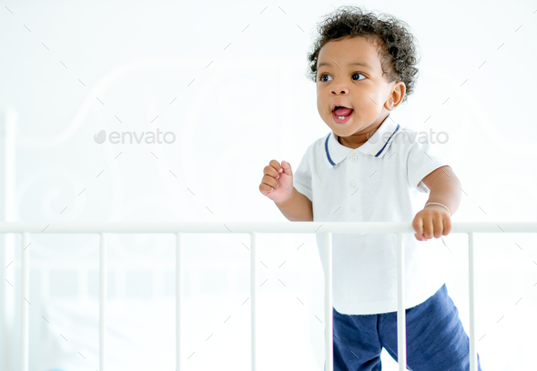 African American child boy stand near bed rail and he look happy by smiling