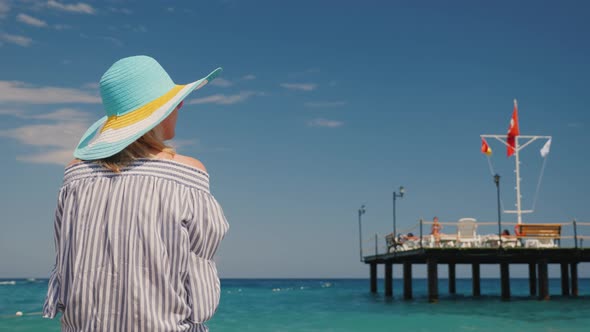 A Woman Admires the Beautiful Sea, Rear View. It Stands Near the Pier with a Raised Turkish Flag alt
