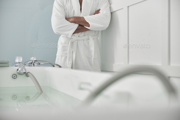 Ppatient in white bathrobe stands by hydro massage tub in spa salon