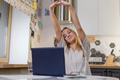 Young relaxed woman sitting in kitchen with laptop in front of her stretching her arms above. - PhotoDune Item for Sale
