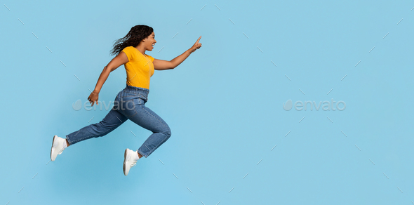 Excited black lady jumping towards copy space