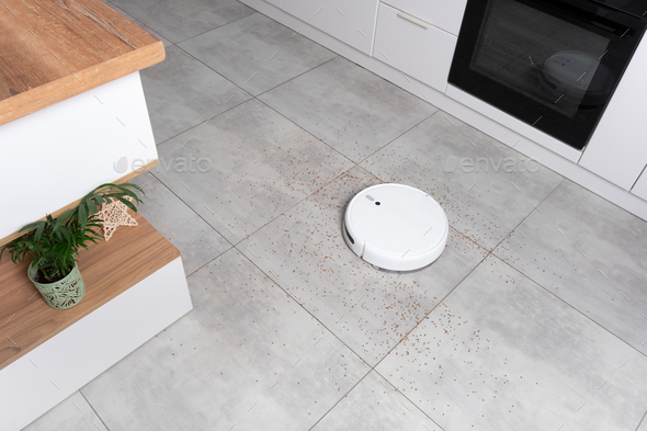Washing White robot vacuum cleaner on a concrete tile floor cleaning dust