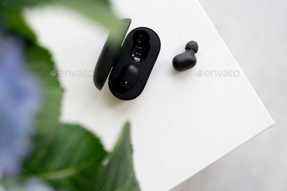 Black wireless earphone close-up from a charger on a white table. portable gadget headphone. Flowers