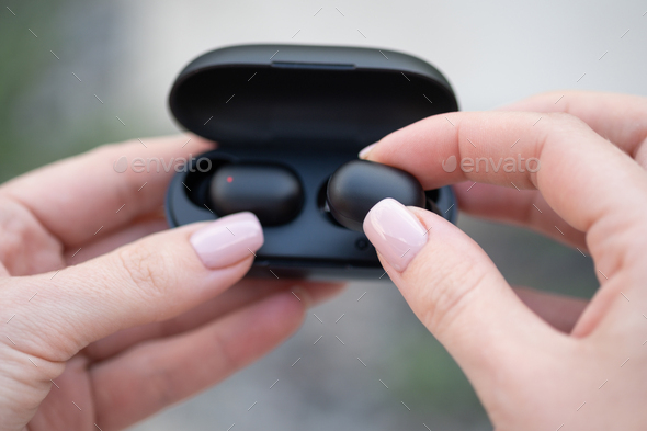 Close-up of a woman taking out a black wireless earbud from his charging box. Female hands