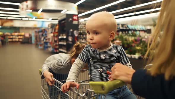 Young Mother Rolls Two Children in a Shopping Trolley on the Store