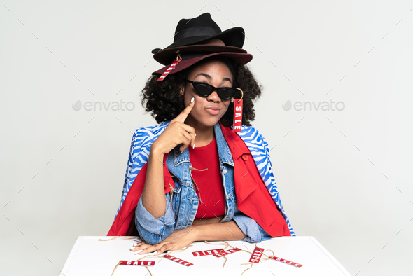 Black woman pointing finger at her cheek while posing with sale labels
