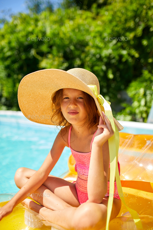 Portrait of little girl in hat relaxing in swimming pool, swims on inflatable  yellow mattress Stock Photo by bondarillia