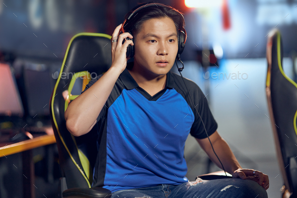 Portrait of confused asian guy, male cyber sport gamer wearing headphones looking at PC screen with