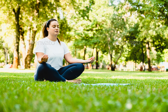 Zen-like fat athlete meditating on yoga class, training in fitness outfit outdoors in city park