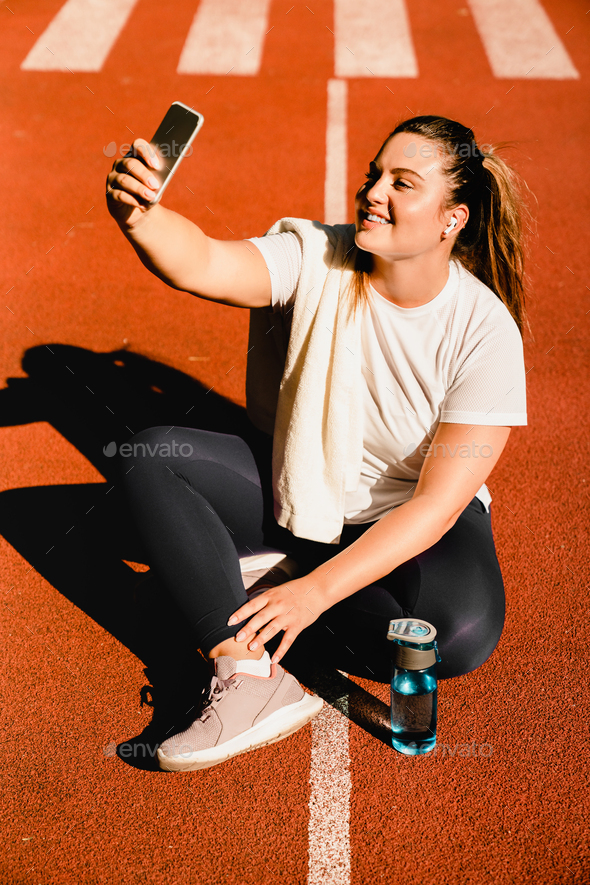Plus-size athlete taking selfie photo on smartphone for social media, having videocall in park