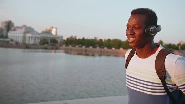 Happy African Man is Walking and Listening to Music By Wireless Headset in City