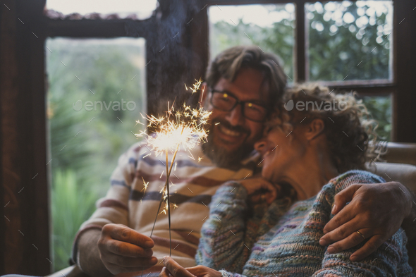 Couple celebrate alone at home with smile and fire sparkler sitting on the couch with outdoor view
