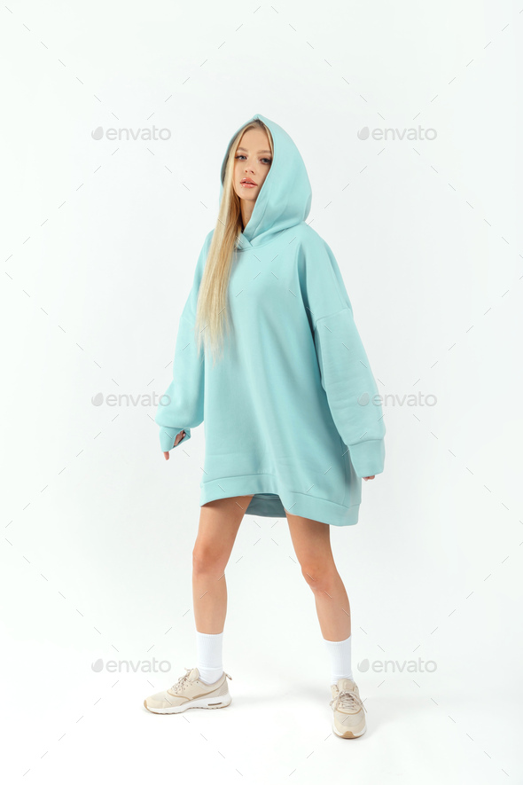 Young pretty woman wearing turquoise hoodie and gray cycling shorts on white background