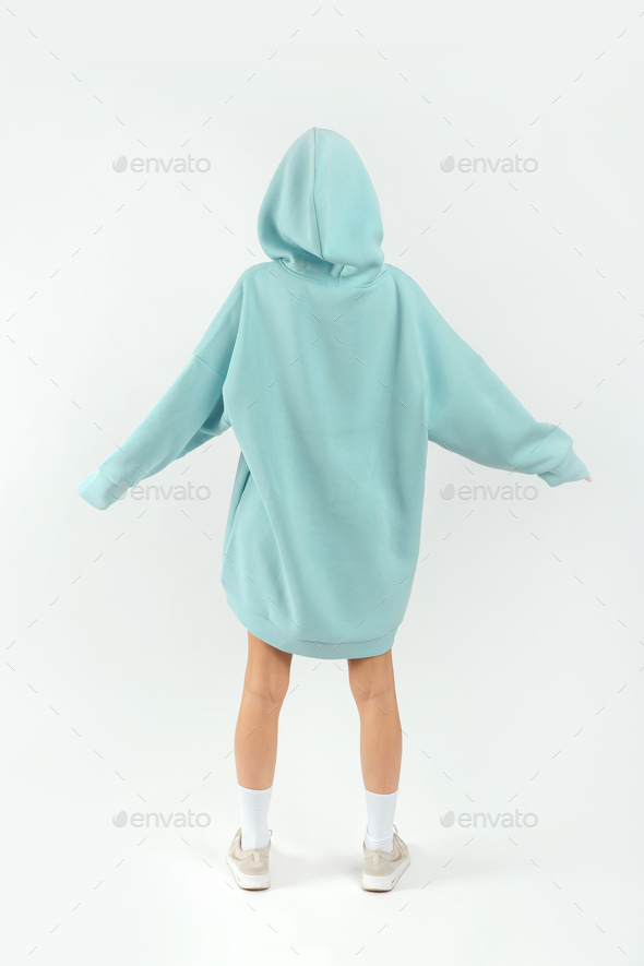 Young pretty woman wearing turquoise hoodie and gray cycling shorts on white background