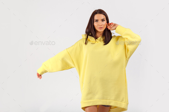 Young pretty woman wearing yellow hoodie and gray cycling shorts on white background