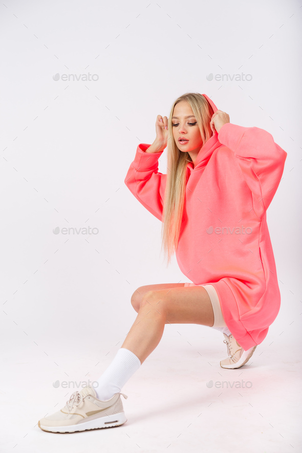 Young pretty woman wearing pink hoodie and white cycling shorts posing on white background