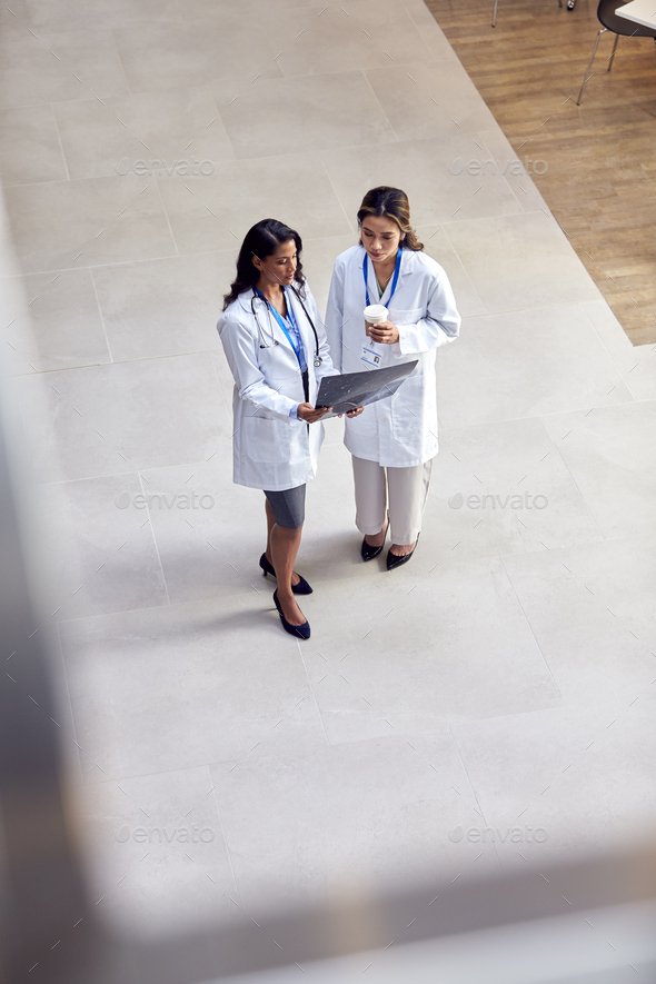Overhead Shot Of Two Female Medical Staff In White Coats Discussing Patient Scan In Busy Hospital