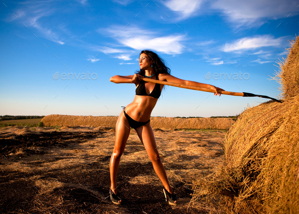 Young woman in black bikini standing outdoors with wooden stick in hand
