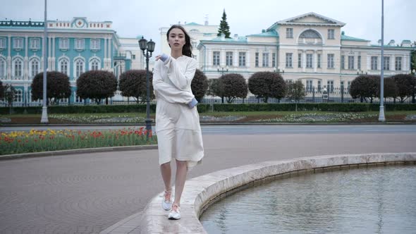 Woman Walks in the City Center on the Edge of the Fountain in the Early Morning
