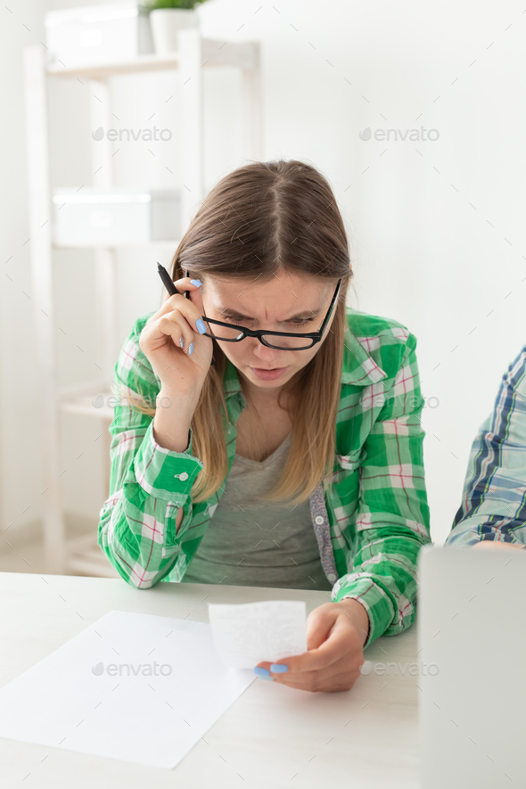 Upset young woman considers the amount of expenses for purchases and payment of credits by entering