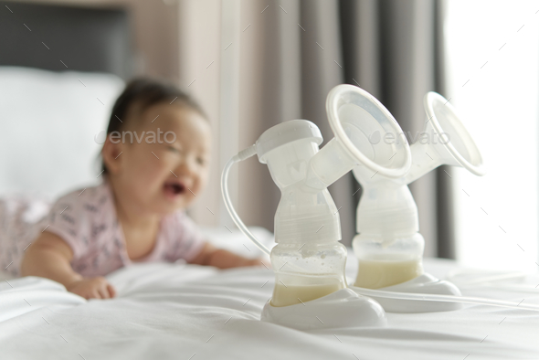 Breast milk in milk pump\'s bottles on the bed with smiling baby crawling in background.