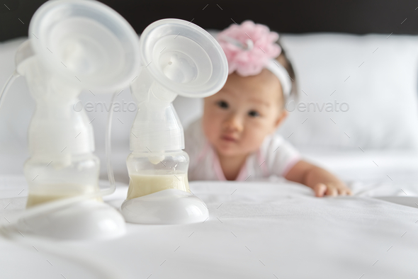 Breast milk in milk pump\'s bottles on the bed with little cute baby crawling in background.