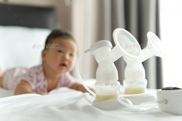 Breast milk in milk pump\'s bottles and pump machine on the bed.