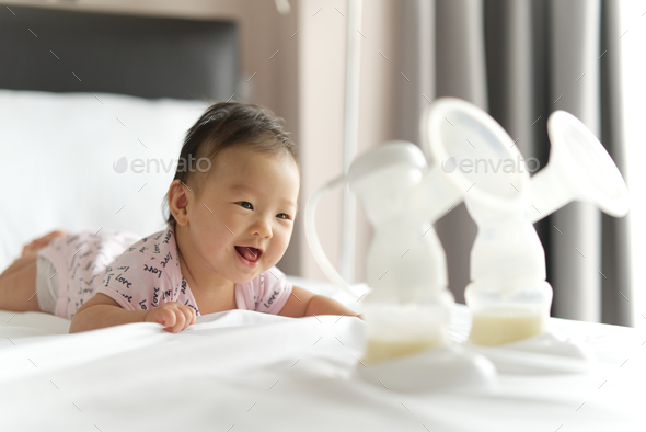Breast milk in milk pump\'s bottles on the bed with selective focus on smiling crawling baby.