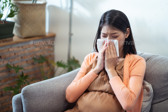 Asian pregnancy woman having a cough and cold fever sitting on sofa at home.