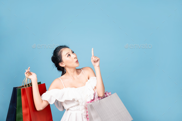 Young pretty cute Asian woman holding shopping bags in both hands with smiley face