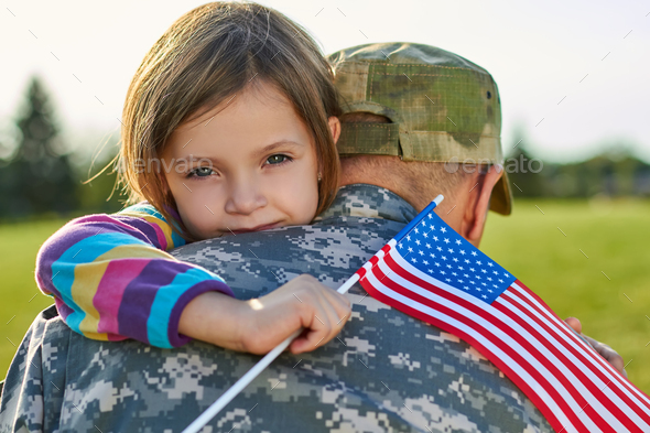 Little girl with US flag is hugging her father.