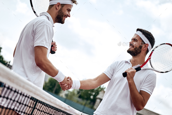 Two men, professional tennis players shake hands before and after the tennis match. One of they has