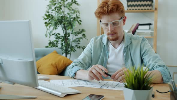 Handsome Gingerhaired Man Architect Working at Home Drawing Plan and Using Computer alt