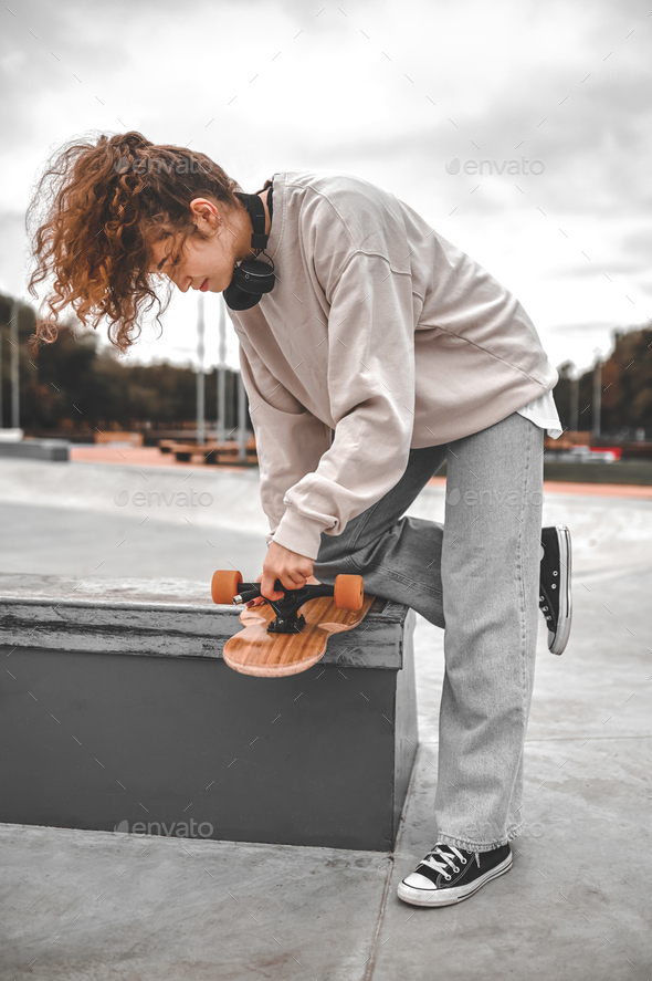 Profile of girl leaning over skateboard adjusting wheel Stock Photo by