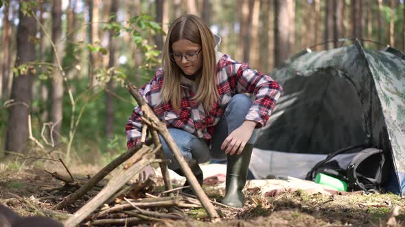 Side View Young Female Traveler Putting Sticks in Triangle Setting Bonfire in Forest alt
