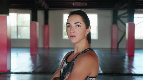 Confident Young Female Fitness Guru Standing in Gym with Arms Crossed and Looking at Camera alt