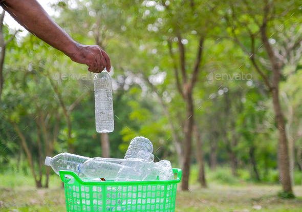 Hands of man throw the bottle to green bin in the garden with concept of safe environment.