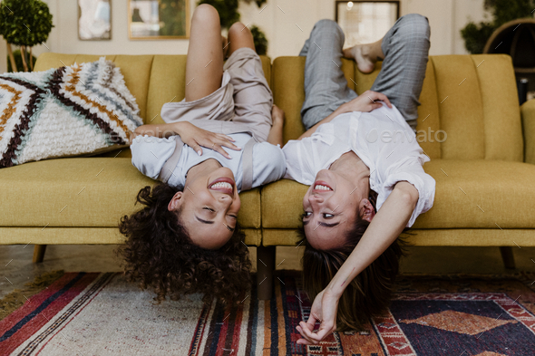Cheerful women lying upside down on a mustard yellow couch