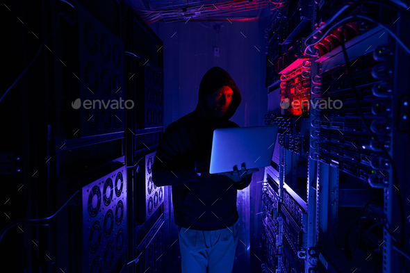 Focused hacker typing on laptop in dark server room