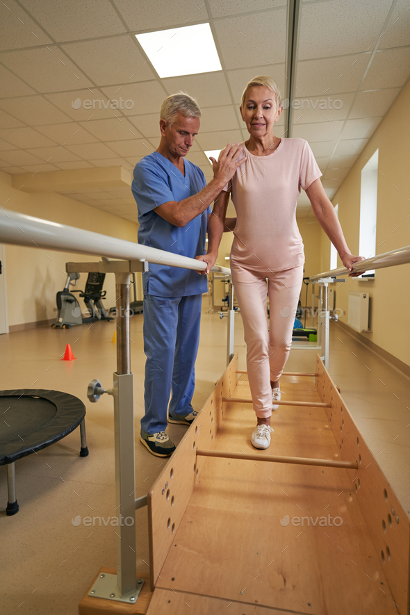 Female patient uses parallel bars to walk in rehab center