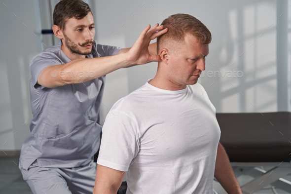 Massage therapist checks posture of man with disability in rehab gym