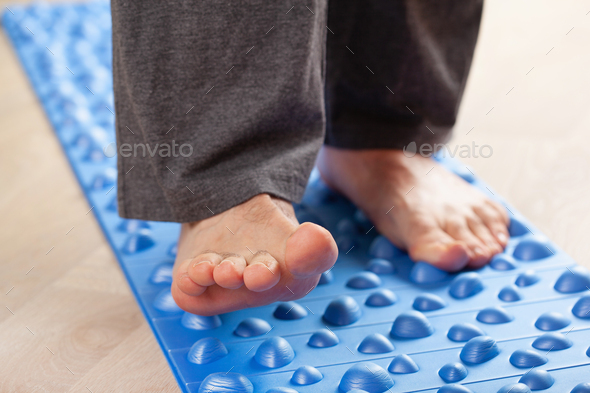 man doing flatfoot correction gymnastic exercise walking on massage mat at home - Stock Photo - Images