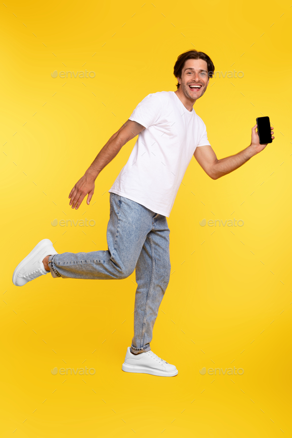 Man showing white empty smartphone screen and jumping up high Stock