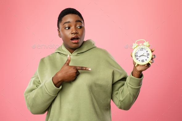 Black Woman Pointing Finger At Clock Standing Over Pink Background