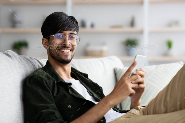 Positive arabic guy playing mobile games at home