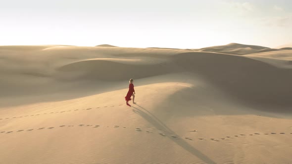  Aerial View of a Girl Walking To the Peak of Sand Dunes on a Windy Day alt