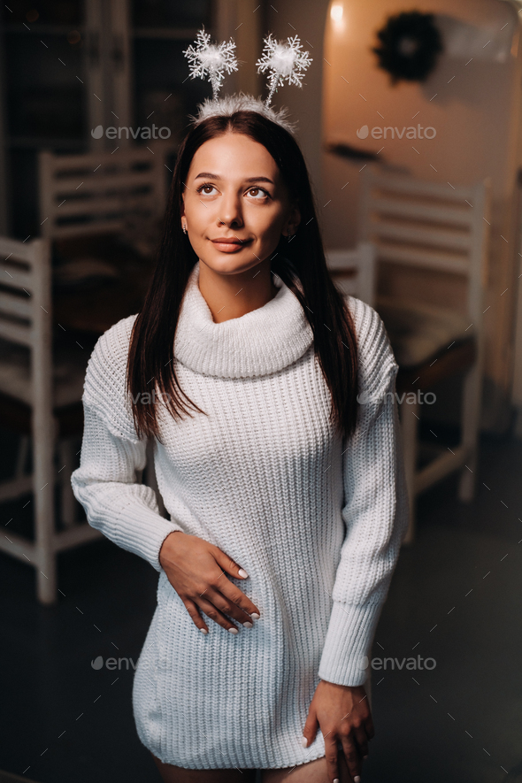 Girl At Christmas With Horns In The Home Interiora Woman On New Years Eve In A White Sweater 