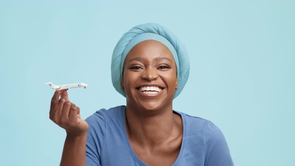 African American Lady Playing With Plane Toy Over Blue Background alt