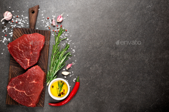 Slices of medium rare roast beef meat on wooden cutting board, pepper and  rosemary branches on wooden background. Top view. Gourmet food. Raw meat  beef steak. Stock Photo