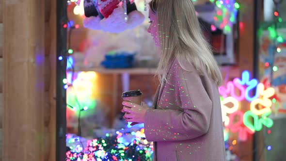 girl in warm clothes with a cup of hot coffee chooses gifts at the Christmas fair.